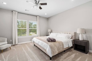 A bedroom with a bed, two bedside lamps, a ceiling fan, and a window with curtains. - New Build 2-Story Townhome/Single Master Suite (Houston)