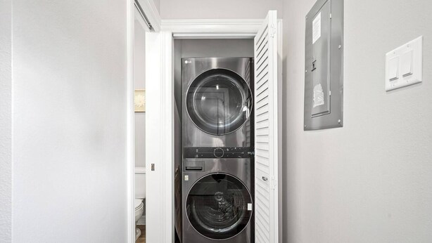 A laundry room with two stacked front-loading washers and dryers, a white door, and a light switch on the wall. - New Build 2-Story Townhome/Single Master Suite (Houston)