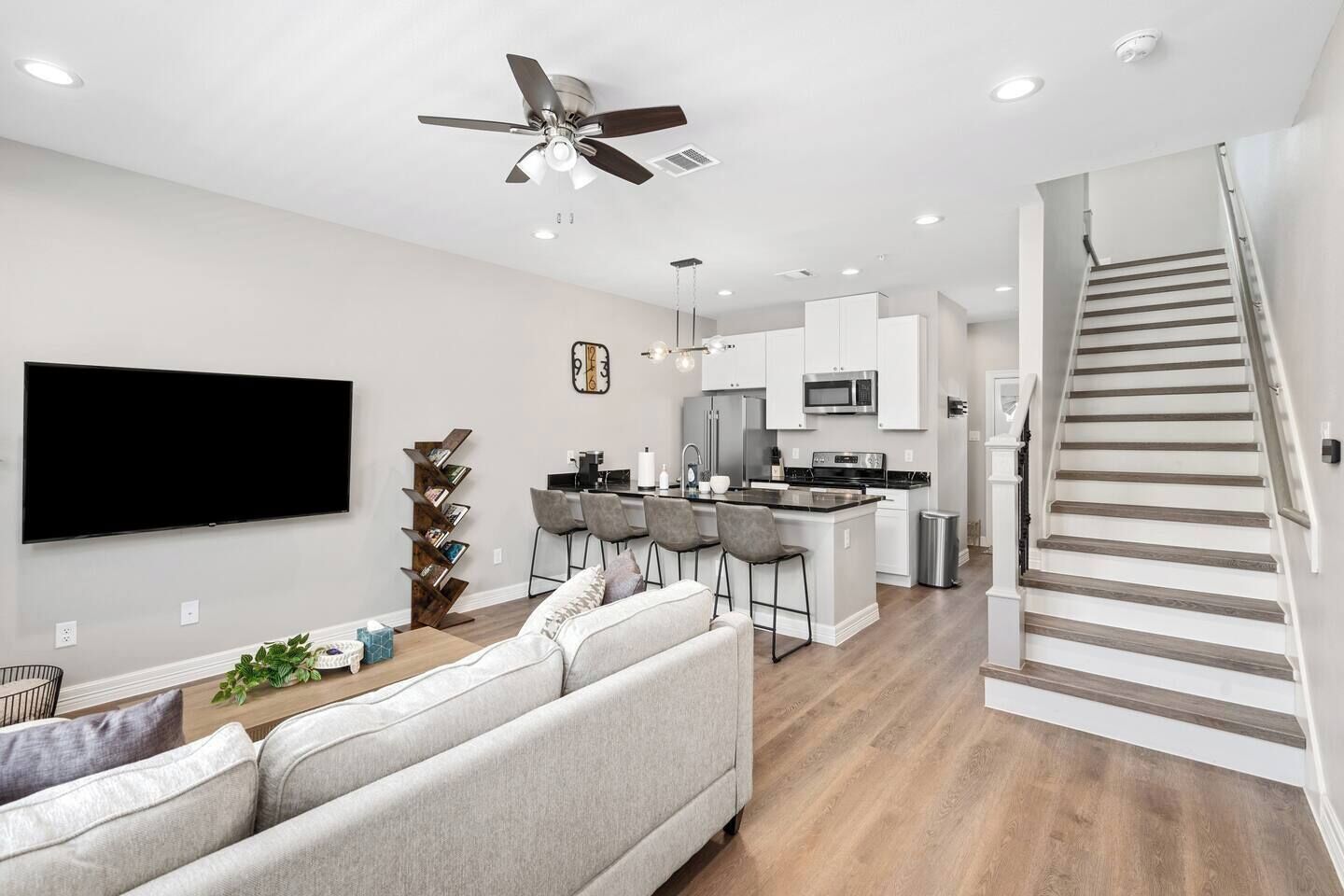 A modern kitchen with a central island, a dining area with bar stools, a living room with a sofa, and a staircase.