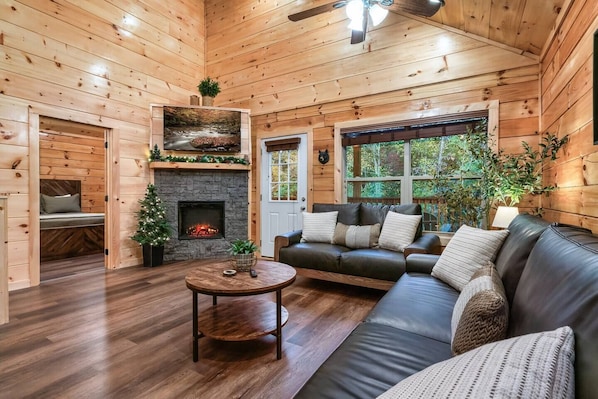 Ein gemütliches Blockhaus-Interieur mit Kamin aus Stein, einer Ledersofa und einem Weihnachtsbaum.