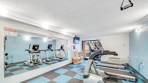 Ein Fitnessstudio mit Laufbändern, Crosstrainern und einer Spiegelwand.