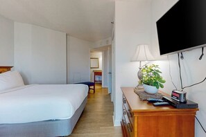 A hotel room with a bed, a desk with a lamp, a television, and a plant. - Carolinian Beach Resort 1833 (Myrtle Beach)