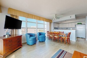 Ein modernes Wohnzimmer mit Flachbildfernseher, einer Holzkommode und einem Essbereich mit Holztischen und -stühlen.