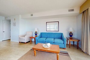 A living room with a blue sofa, a beige armchair, a wooden coffee table, and two lamps on side tables. - Carolinian Beach Resort 1833 (Myrtle Beach)
