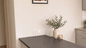A kitchen with a grey countertop, a framed picture on the wall, a potted plant, and a lit candle. - Nordhaven Sundbyberg (sundyberg)