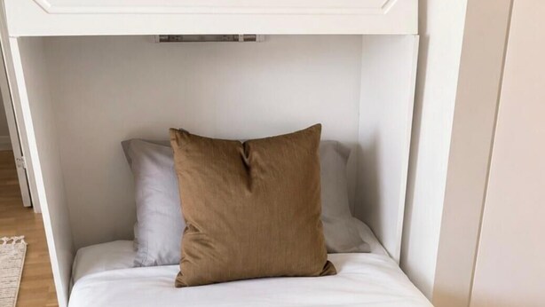 A compact bed with a headboard, a grey blanket, and two pillows. - Nordhaven Sundbyberg (sundyberg)