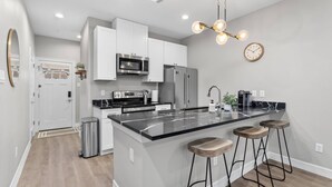 A modern kitchen with a central island, stainless steel appliances, and bar stools. - Newly Built 2-Story Townhome: Single Master Suite (Houston)