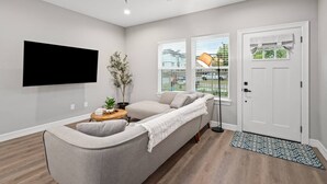 A modern living room with a sofa, a flat-screen TV, a ceiling fan, and a door with a window. - Newly Built 2-Story Townhome: Single Master Suite (Houston)