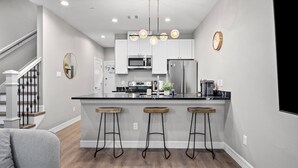 A modern kitchen with a central island, bar stools, a stainless steel refrigerator, and a microwave. - Newly Built 2-Story Townhome: Single Master Suite (Houston)