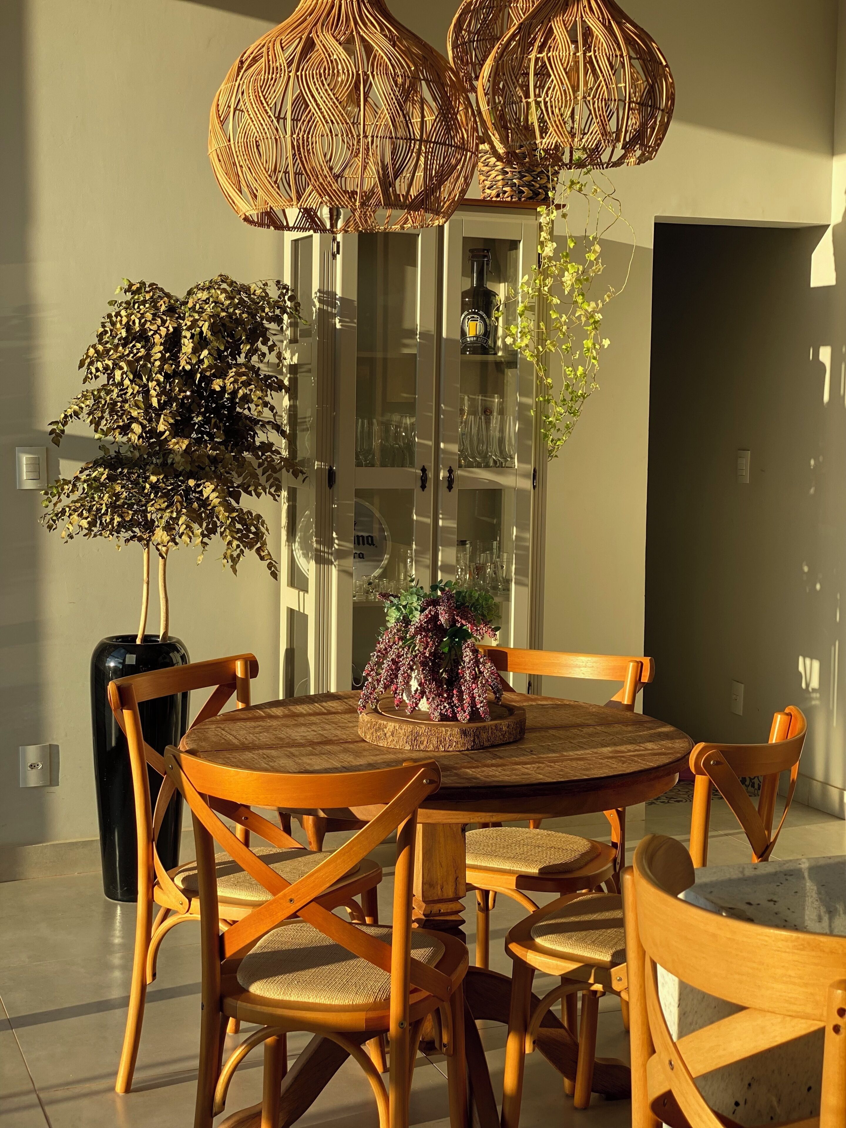 Ein Essbereich mit einem runden Tisch, Holzstühlen, einem Blumentopf und einer Vitrine mit Regalen.
