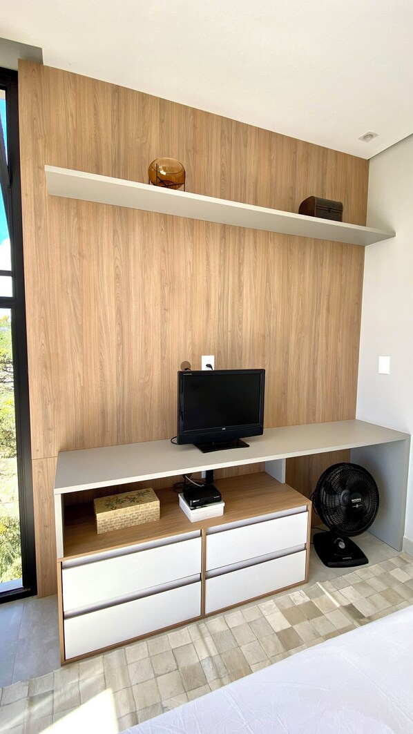 A modern living room with a flat-screen TV, wooden shelves, a fan, and a white sofa.