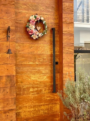 Pared de madera con una corona decorativa, un picaporte negro y una campana.