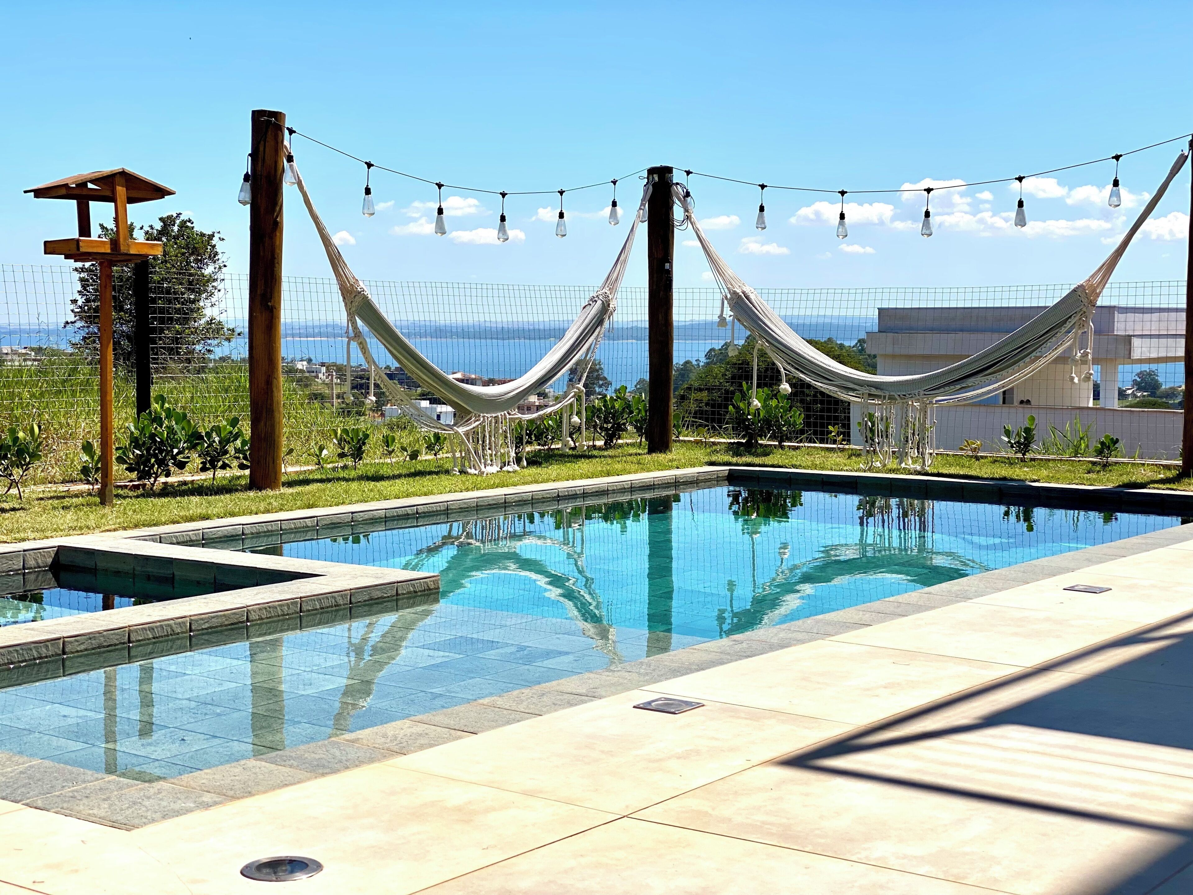 A swimming pool with a hammock and string lights, surrounded by a fence and greenery.