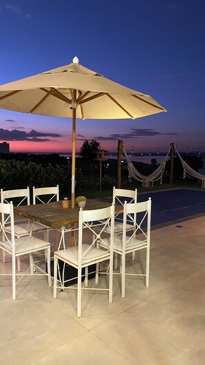 An outdoor patio with a table and chairs, a large umbrella, and a view of the sunset.
