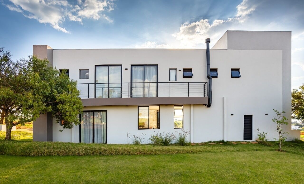 Une maison moderne à deux étages, dotée d’un toit plat, de grandes fenêtres et d’un balcon.