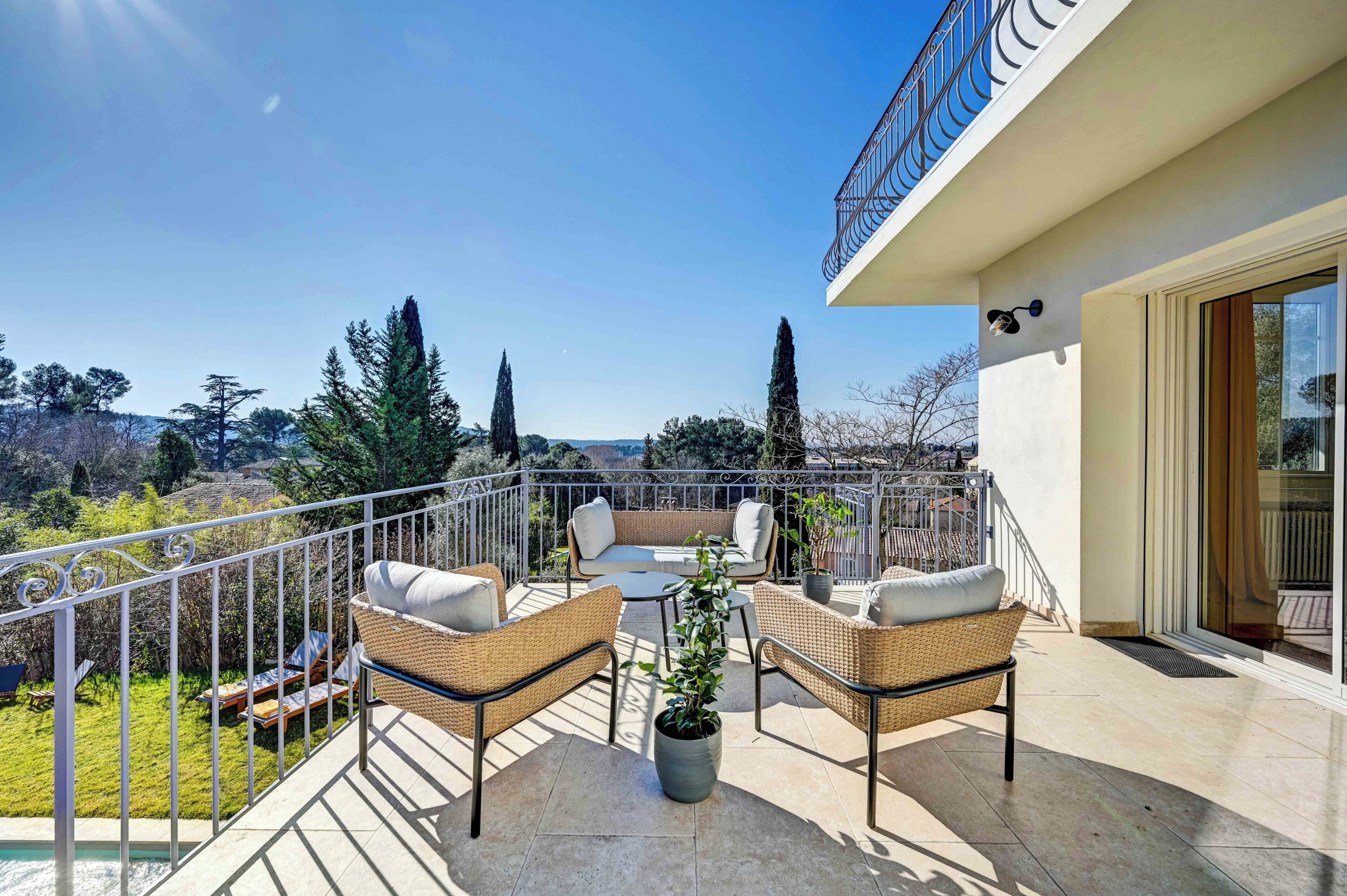 A balcony with wicker furniture, a potted plant, and a view of the surrounding landscape.