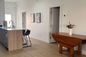 A modern kitchen with a wooden island, bar stools, and a dining table. - New 3BR Lake Country Home | Golf, Wine, Lakes & Mountain Getaway (Kelowna)