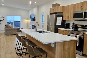 A modern kitchen with a central island, bar stools, stainless steel appliances, and wooden cabinets. - New 3BR Lake Country Home | Golf, Wine, Lakes & Mountain Getaway (Kelowna)
