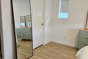 Ein Schlafzimmer mit Holzboden, einem Kleiderschrank, einem Bett und einem Fenster mit Jalousien.