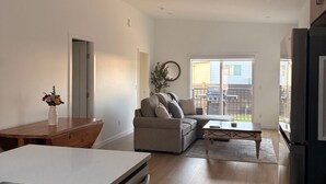 Ein modernes Wohnzimmer mit einem Ecksofa, einem Esstisch und einer Küchenzeile inklusive Kühlschrank.