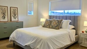 Ein ordentlich eingerichtetes Schlafzimmer mit einem Bett, Nachttischen und Blick durch ein Fenster.