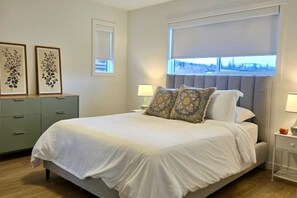A neatly arranged bedroom with a bed, bedside tables, and a view through a window. - New 3BR Lake Country Home | Golf, Wine, Lakes & Mountain Getaway (Kelowna)