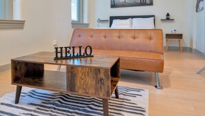 Un salón moderno con un sofá de cuero, una mesa de centro de madera con un letrero que dice 'HELLO' y una alfombra a rayas.