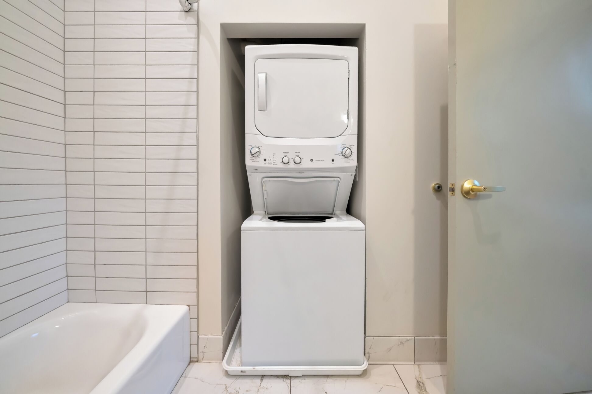 Eine kompakte Waschmaschine und Trockner in einem Badezimmer mit einer Badewanne.