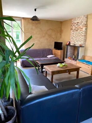 A room with a sofa, a television, a wooden table, and a potted plant.