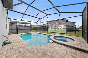 Ein Pool mit Whirlpool, umgeben von einer überdachten Terrasse mit Blick auf ein Fußballspiel auf einem großen Bildschirm.