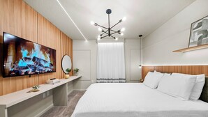 Een moderne hotelkamer met een groot bed, een flatscreen televisie bevestigd aan een houten wandpaneel, een nachtkastje met een spiegel en een plafondlamp.
