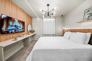 A modern hotel room with a large bed, a flat-screen TV mounted on a wooden panel wall, a bedside table with a mirror, and a ceiling light fixture. - 8BR house sleeps 22 with spa in kissimmee (Kissimmee)