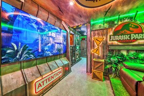 A themed interior with a large screen displaying a jungle scene, a sign reading 'ATTENTION', and a 'JURASSIC PARK' sign. - 8BR house with pool table near Disney area (Kissimmee)
