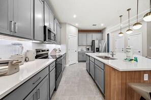 A modern kitchen with grey cabinets, stainless steel appliances, and a white countertop. - 8BR house with pool table near Disney area (Kissimmee)