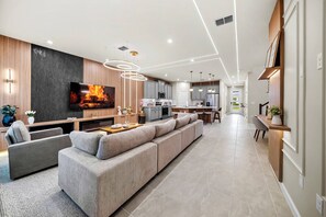 A modern living room with a large flat-screen TV, a sofa, and a dining area with a kitchen in the background. - 8BR house sleeps 22 with spa in kissimmee (Kissimmee)