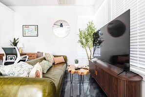 Un salon moderne comprenant un canapé, une table basse, un téléviseur, un bureau avec une chaise et une horloge murale.