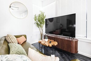 Ein modernes Wohnzimmer mit einer Couch, einem Couchtisch, einem Fernseher und einer Pflanze.