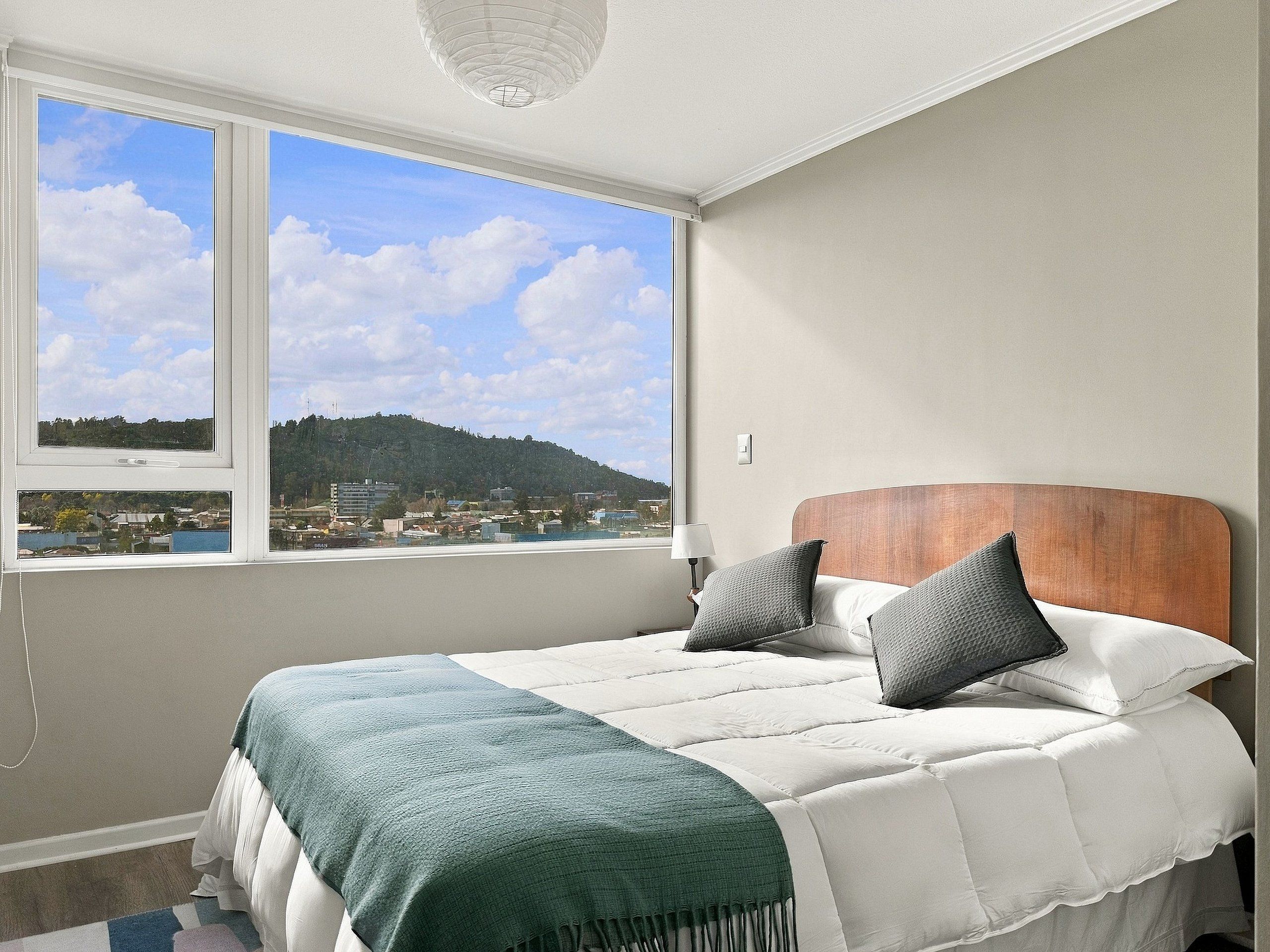 Un dormitorio con cama, ventana con vista a paisaje urbano y lámpara en la mesita de noche.