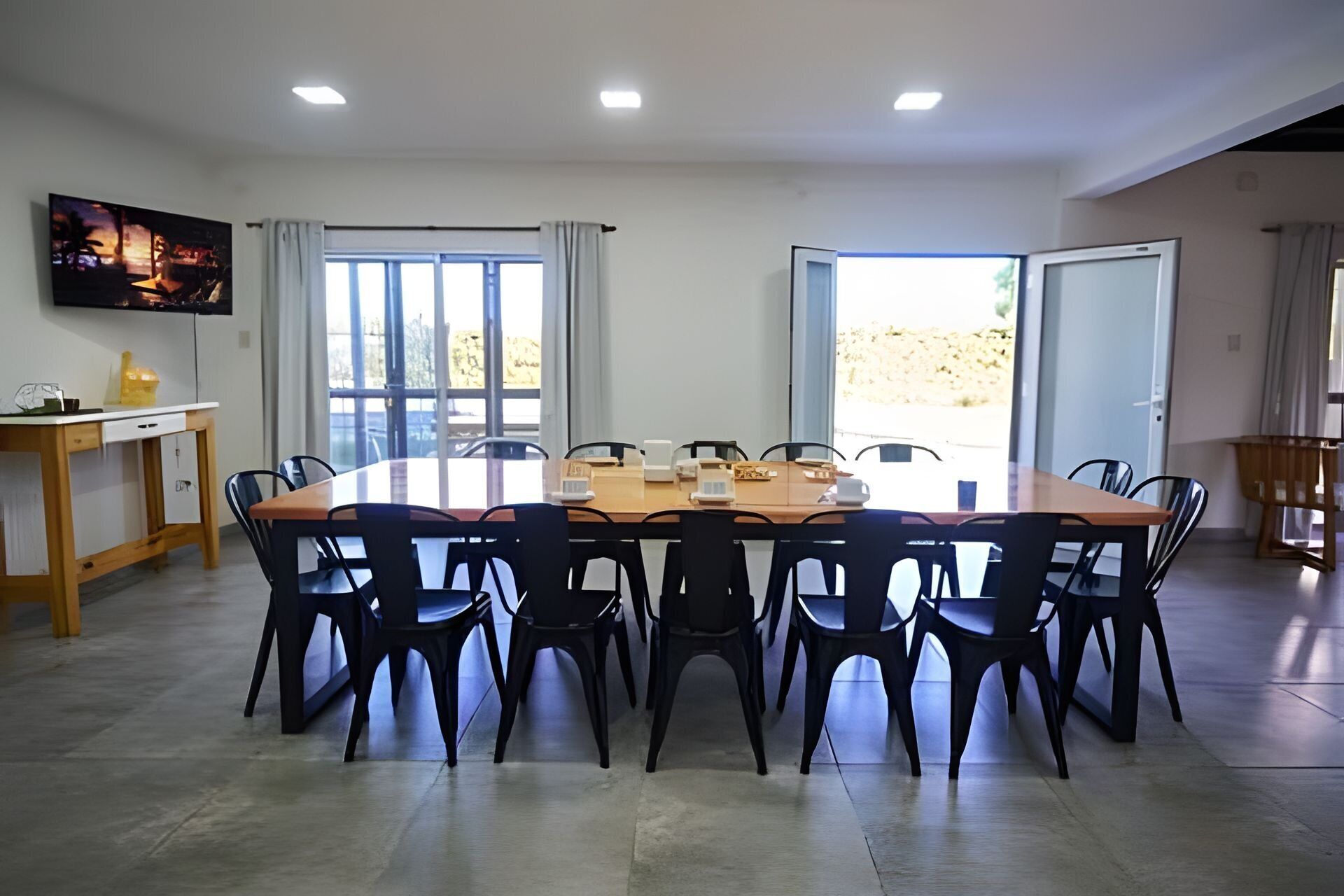 Une salle de conférence avec une table ronde, des chaises noires, un bureau en bois, un téléviseur et de grandes fenêtres.
