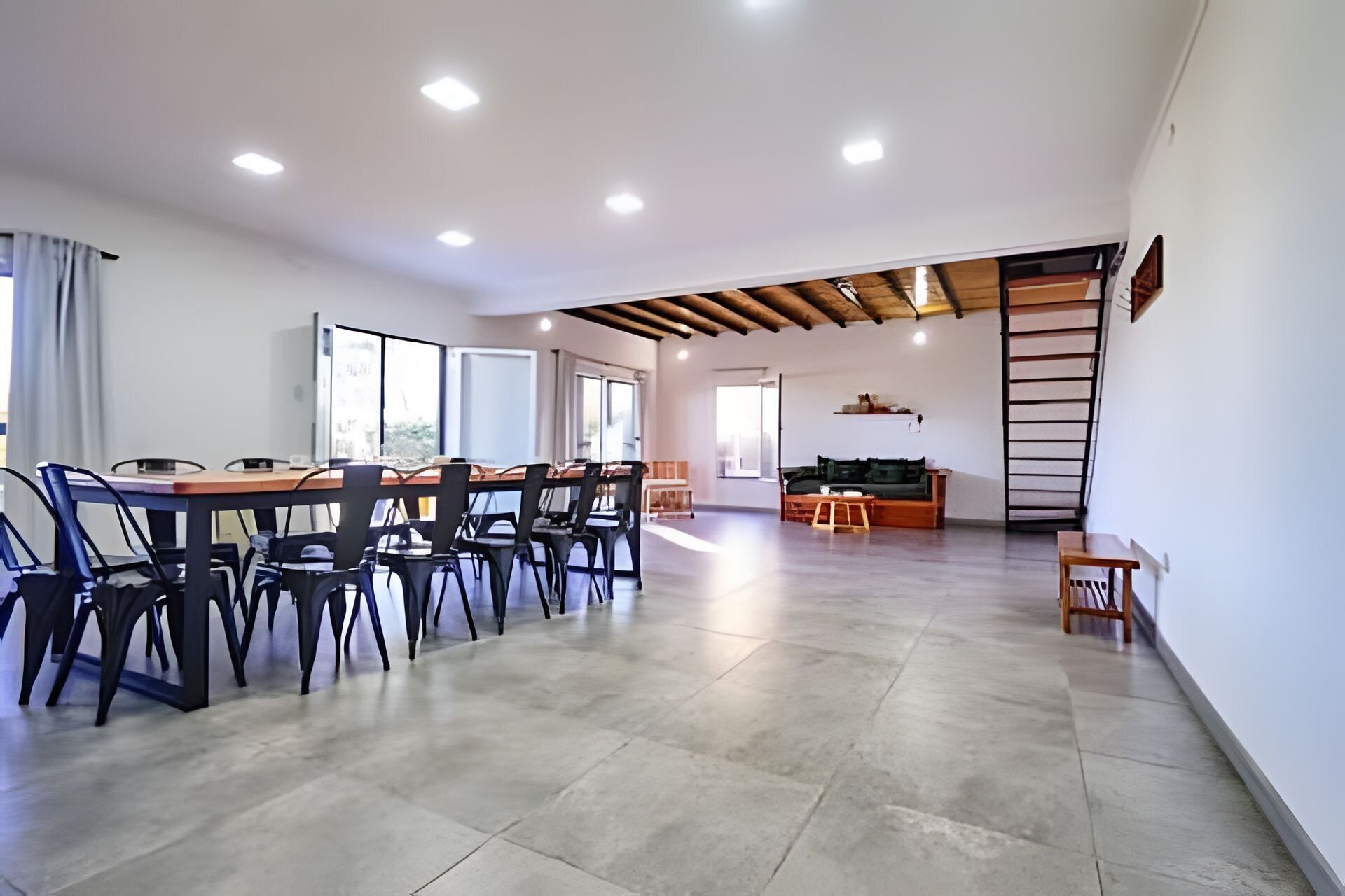 Una habitación amplia con una mesa de comedor y sillas, un sofá y una escalera apoyada en la pared.