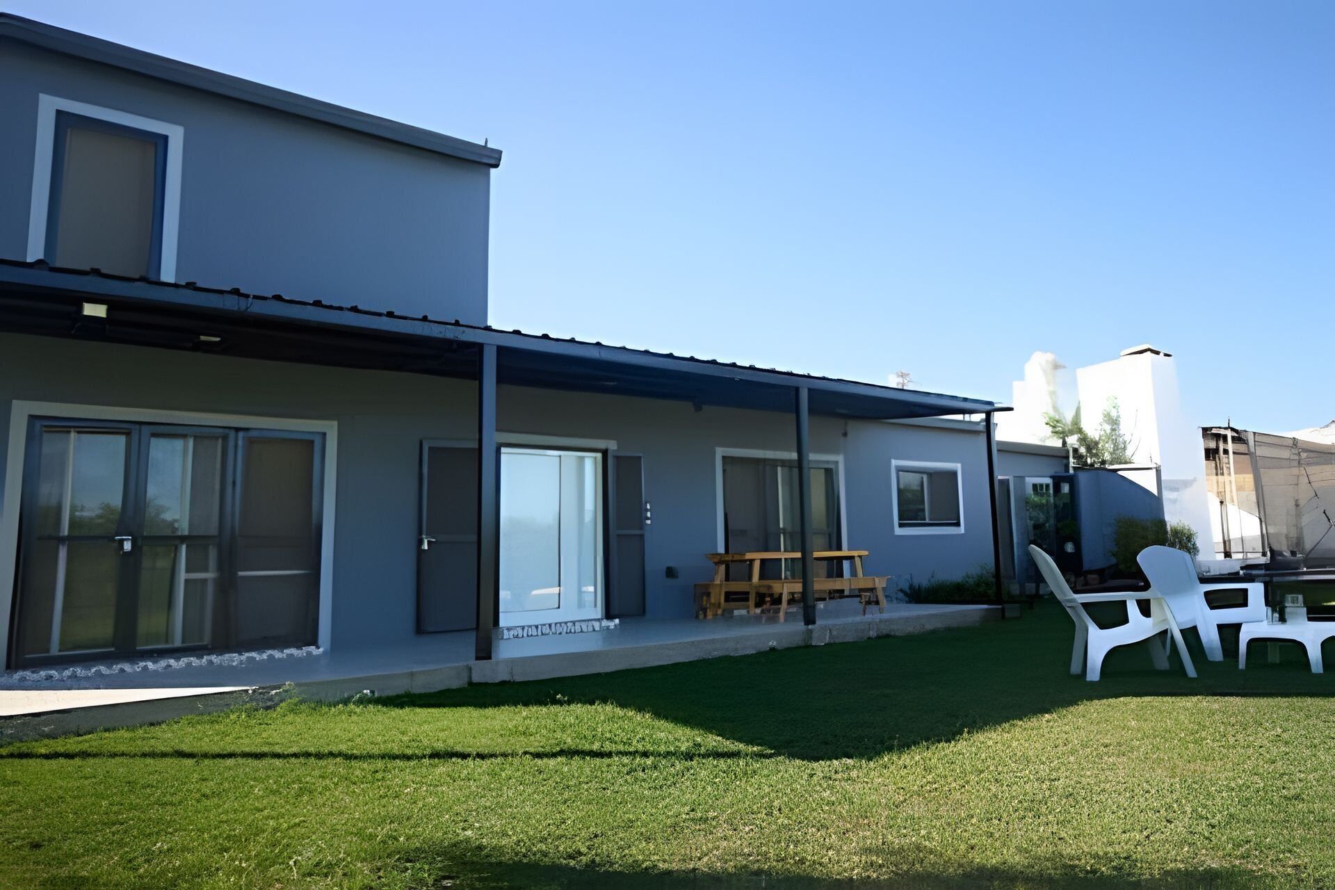 Ein modernes, zweistöckiges Haus mit überdachter Terrasse, großen Schiebegläsern und einem gepflegten Rasen.