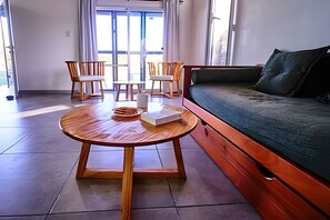 Un salon moderne avec une table ronde en bois, deux chaises, un canapé et une grande fenêtre.