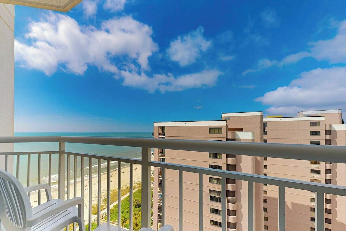 Een balkon met uitzicht op een strand en hoge gebouwen.