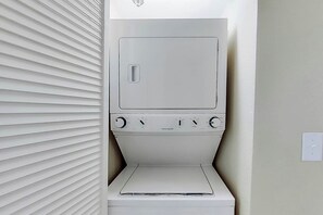 A compact, white laundry room with a built-in washer and dryer, a small control panel, and a vented cabinet. - Carolinian Beach Resort 1836 (Myrtle Beach)