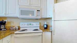 Una cocina con armarios blancos, microondas, estufa y refrigerador.