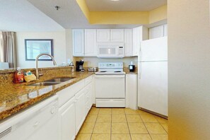 A compact kitchen with white cabinets, a granite countertop, a stainless steel sink, a microwave, a stove, and a refrigerator. - Carolinian Beach Resort 1836 (Myrtle Beach)