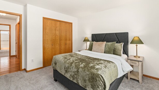 A bedroom with a bed, bedside lamps, a wooden door, and a hallway leading to another room.