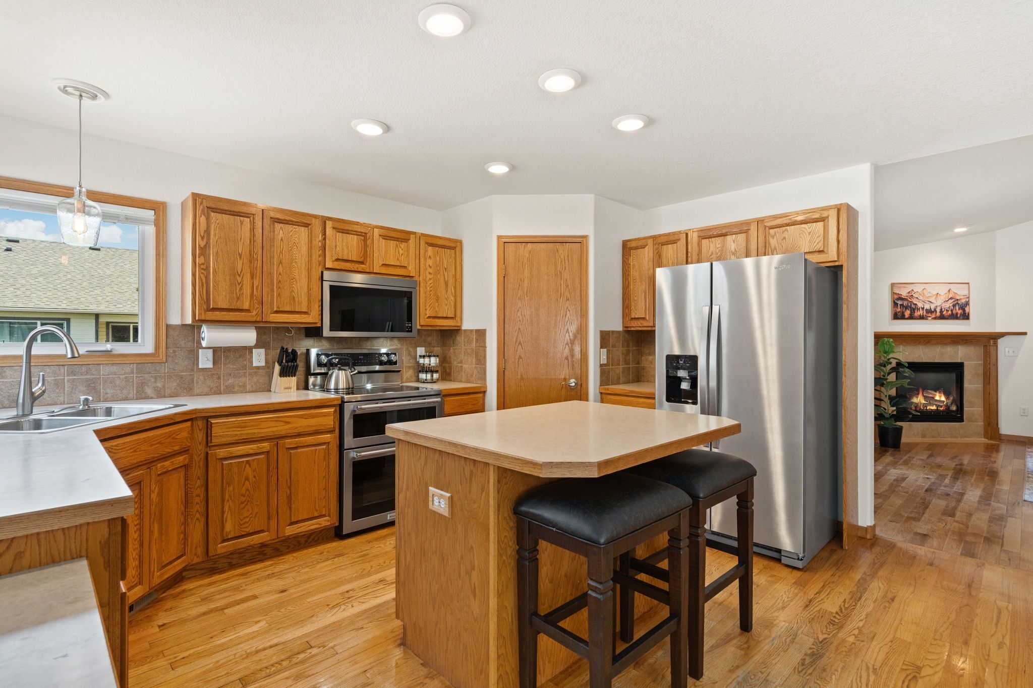 A modern kitchen with wooden cabinets, stainless steel appliances, a central island, and a fireplace.
