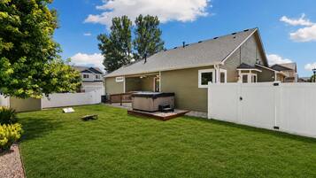 A residential backyard with a hot tub, a wooden deck, and a white fence.