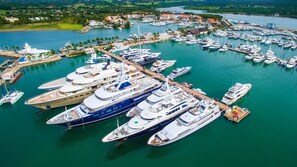 A marina with multiple yachts docked, surrounded by a coastal town with houses and greenery. - Altos de Chavon Luxury Retreat - Casa de Campo Resort (La Romana)